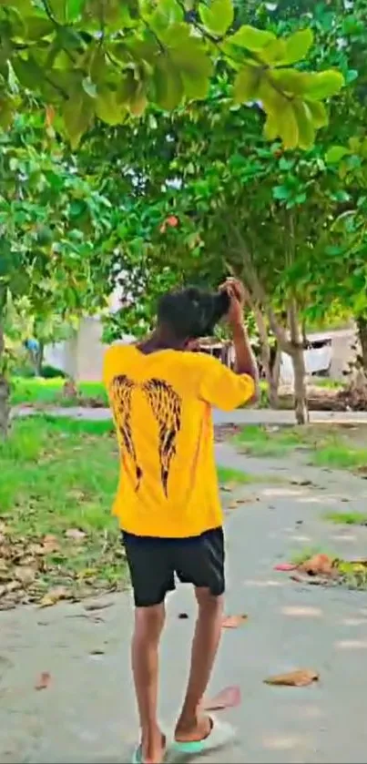 Person walking on a leafy path, wearing a yellow shirt.