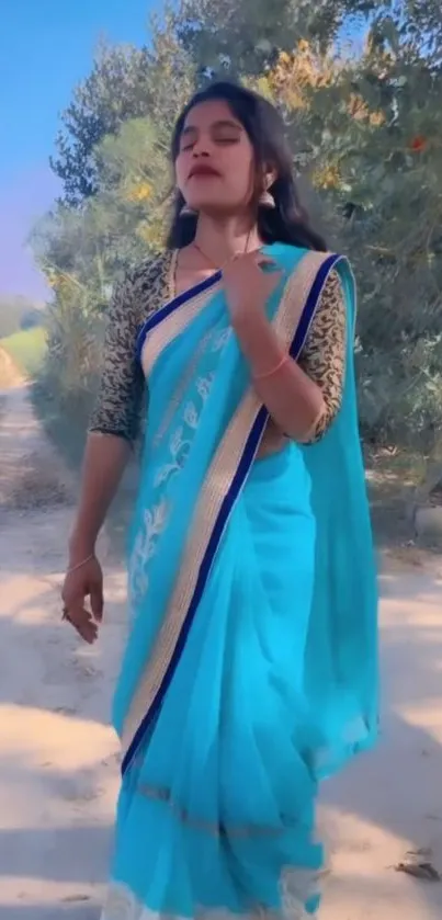 Woman in blue saree walking down a serene, tree-lined path.