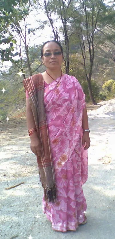 Woman in pink sari standing on a scenic outdoor path with trees.