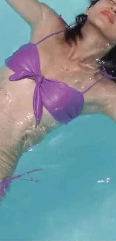 Woman relaxing in pool wearing a purple swimsuit.