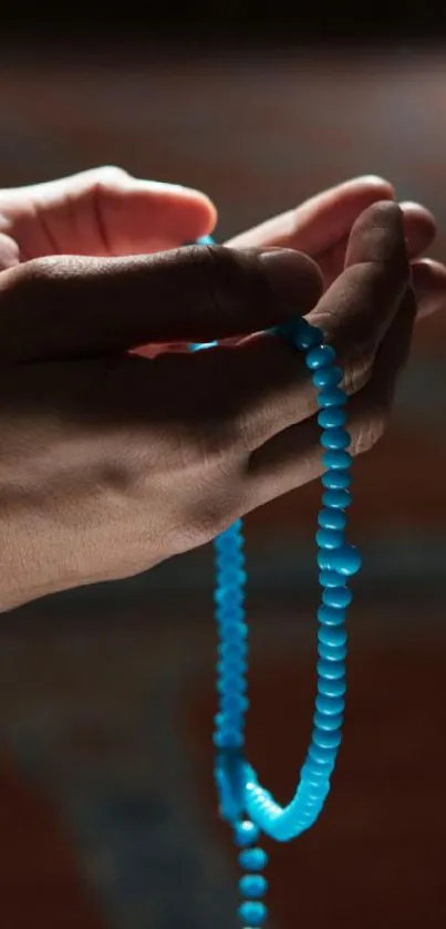 Hands holding blue prayer beads in soft lighting.