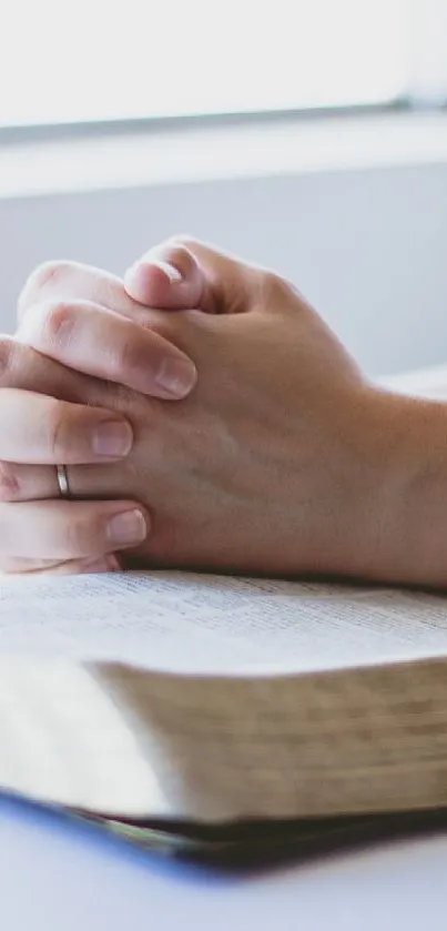 Person praying with hands over an open book in soft light.