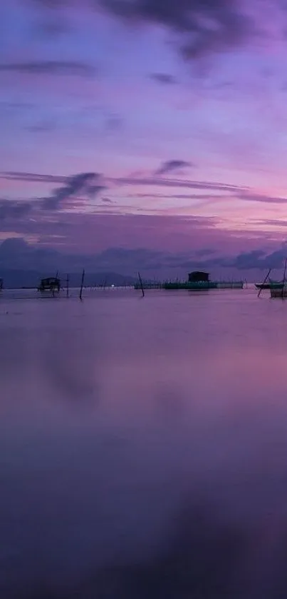 Purple sunset over calm ocean with silhouetted structures.