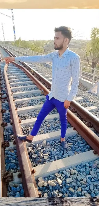 Man standing on railway tracks at sunset with ocean backdrop.