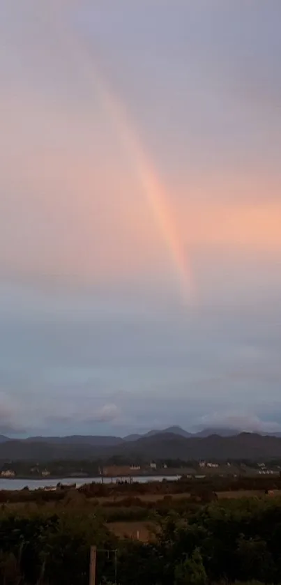 Rainbow over mountains with pastel sky.