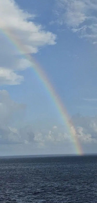 Rainbow arching over the peaceful ocean with cloudy sky.