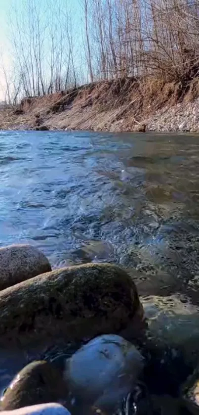 Serene riverbank with tranquil flowing water and rocks, perfect for phone wallpaper.