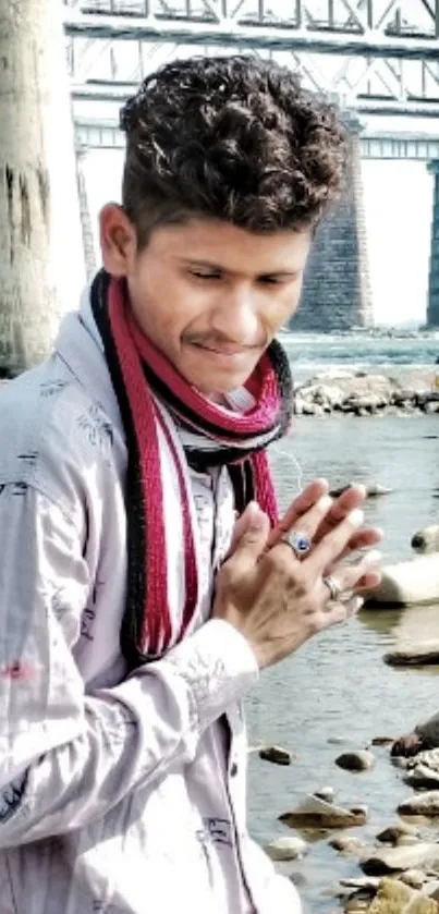 Person standing by a river with a bridge in the background.