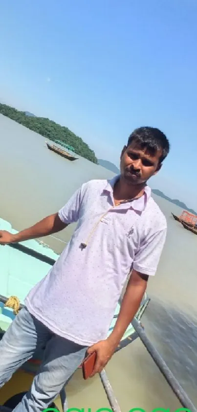 Man standing by a peaceful river with boats under clear blue skies.