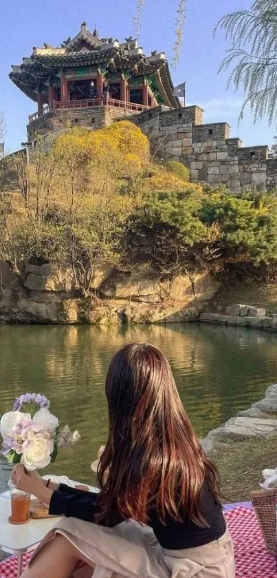 Woman at riverside picnic with scenic traditional architecture.