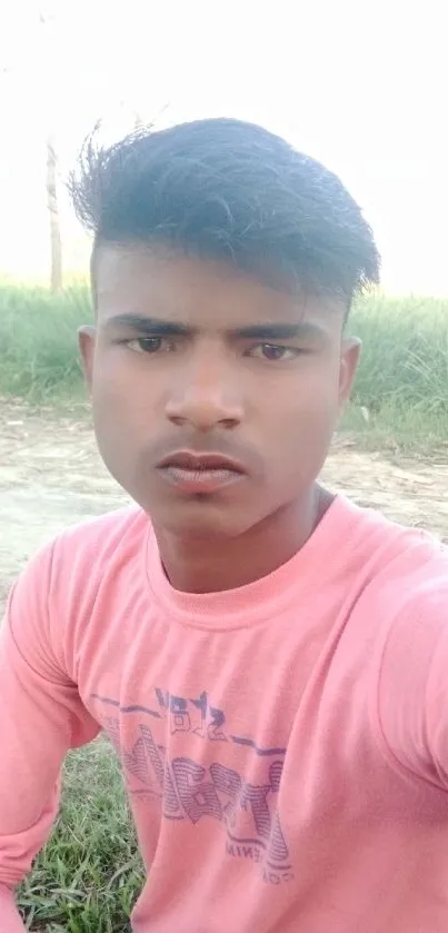 Young individual in a serene rural setting with pink shirt against a field backdrop.