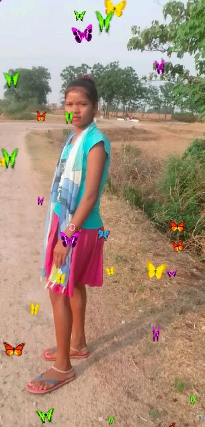 A woman stands on a dirt path in a sunny, rural landscape.