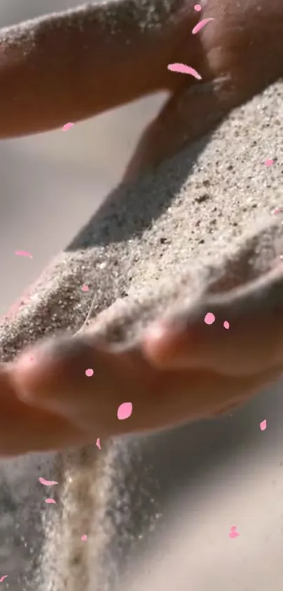 Sand gently flows through a hand, adorned with pink petals.