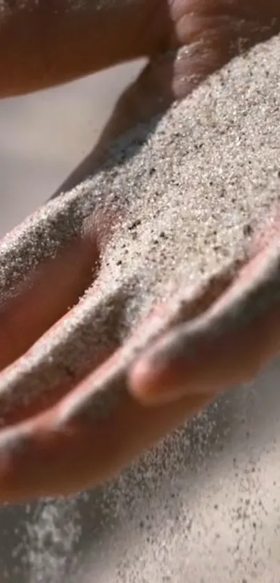 Hand gently holding flowing sand with soft background.