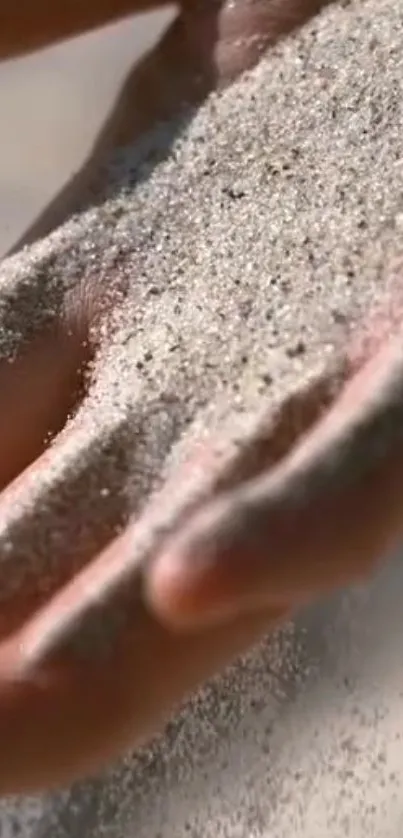 A close-up of a hand letting fine sand fall gracefully through the fingers.