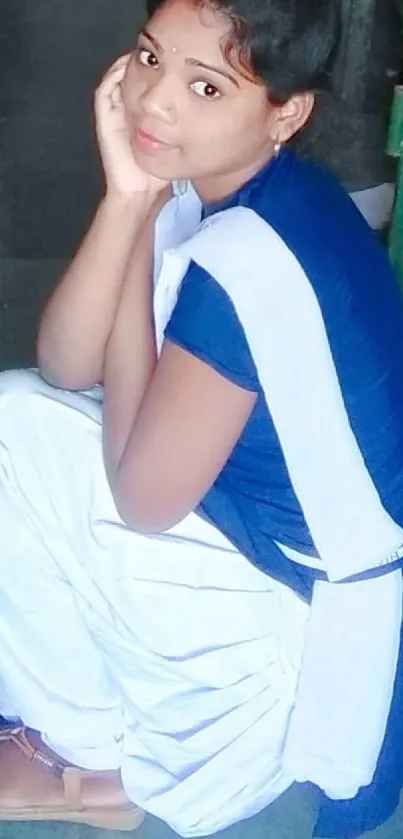 Portrait of a schoolgirl in blue and white attire sitting peacefully.