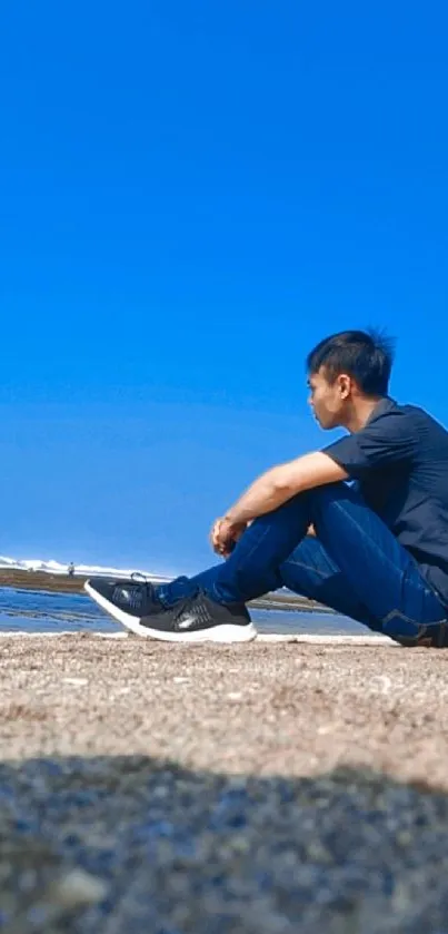 Man sitting by the sea under a clear blue sky.