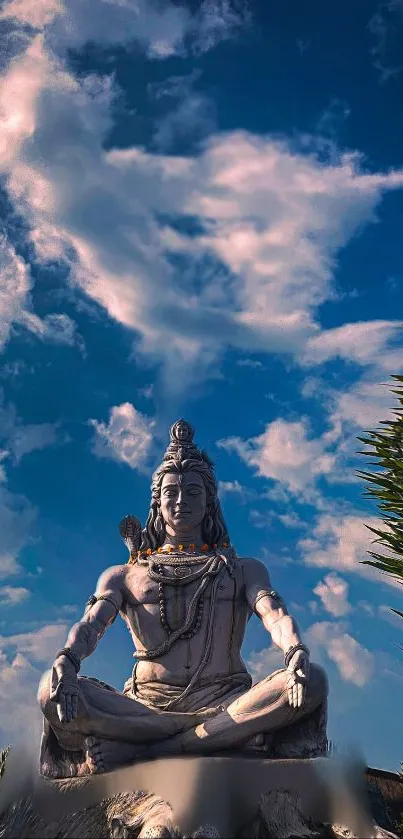 Shiva statue under a vibrant blue sky with clouds and greenery.