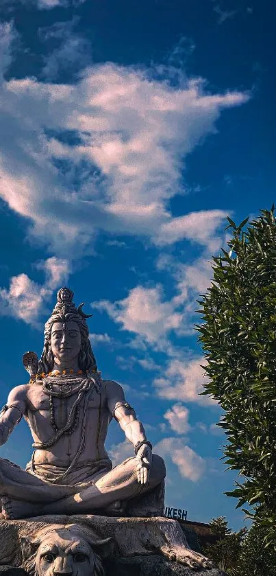 Shiva statue against a vibrant blue sky with clouds and greenery.