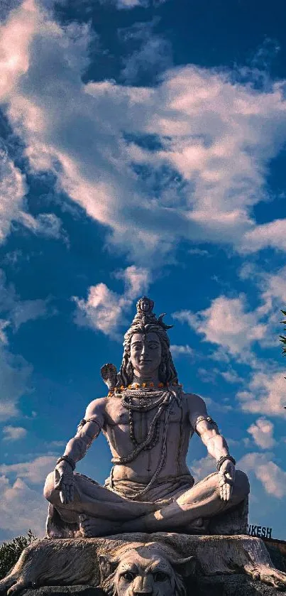 Shiva statue sits peacefully under a bright blue sky with scattered clouds.