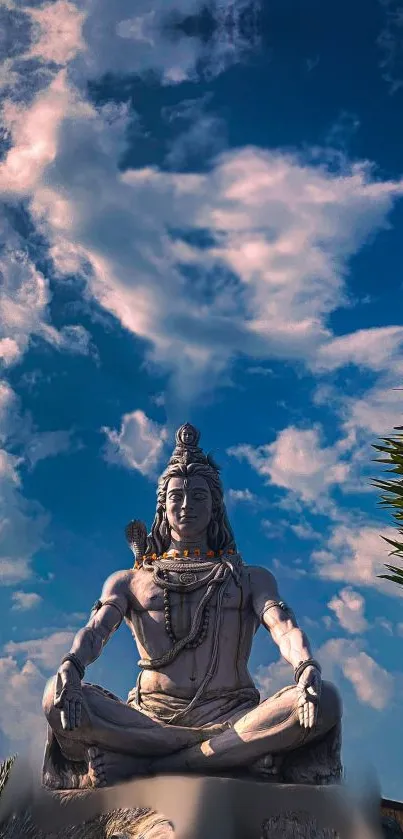 Statue of Lord Shiva meditating under a blue sky with clouds.
