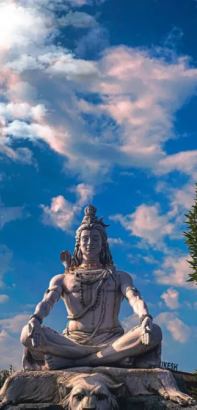 Statue of Shiva under a blue sky with clouds.