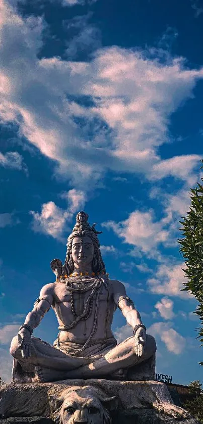 Serene Shiva statue under a vibrant blue sky with fluffy clouds.