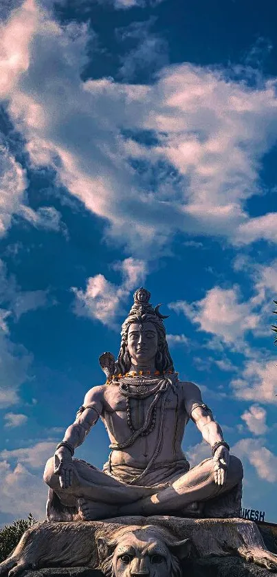 A serene statue of Shiva meditating under a vibrant blue sky with clouds.