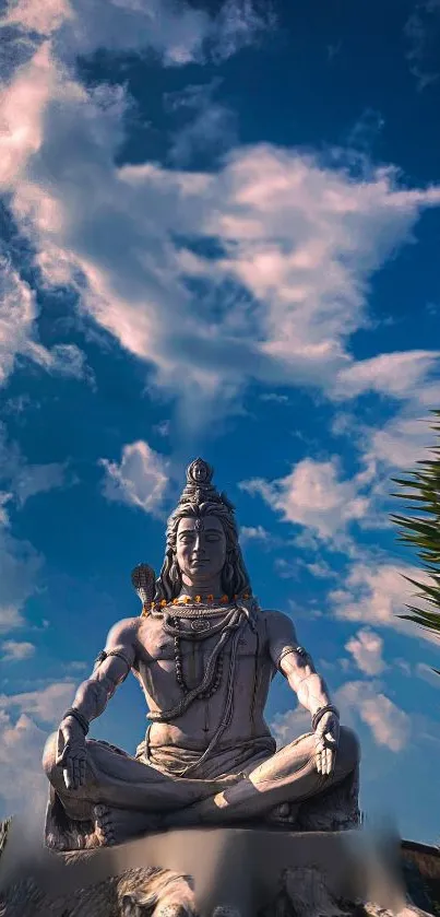 Statue of Shiva meditating under a clear blue sky with clouds.