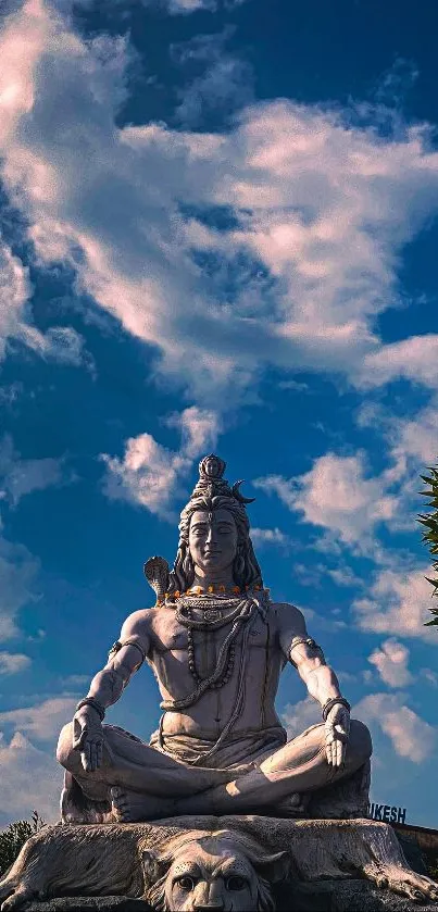 Statue of Shiva against a vibrant blue sky with clouds.