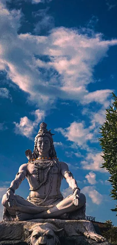 Shiva statue against a vibrant blue sky with fluffy clouds.