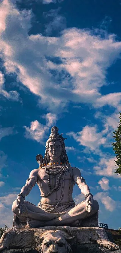Shiva statue under a vibrant blue and cloudy sky, surrounded by greenery.