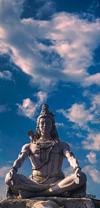 Shiva statue meditation under a vibrant blue sky with soft clouds.