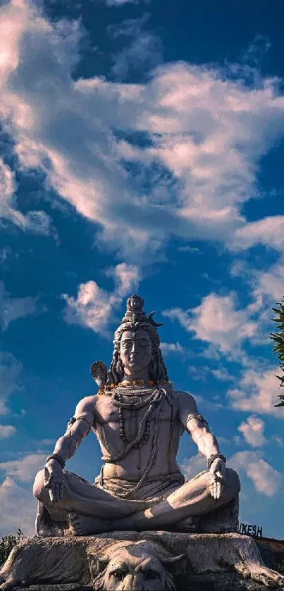 Shiva statue against a vibrant blue sky with fluffy clouds.