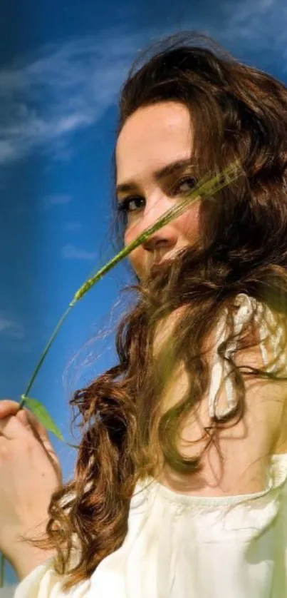 Portrait of a woman with a blue sky background, holding a green leaf.