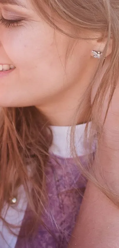 Close-up of a smiling woman with earrings in soft pink lighting.