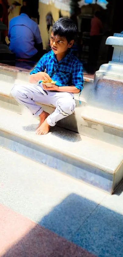 Boy sitting on steps in sunlight, vivid blue shirt