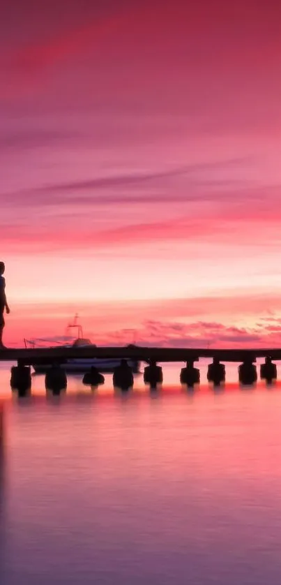 Silhouette on dock with pink sunset sky reflecting on water.