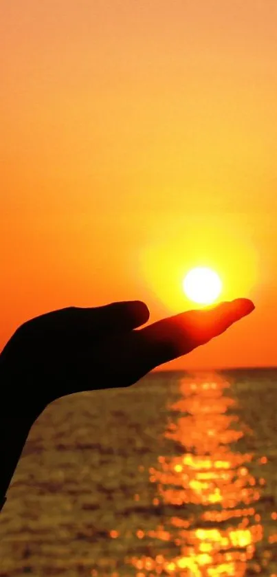 Hand holding the sun at sunset over a calm ocean.