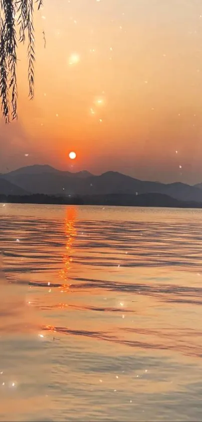 Orange sunset over peaceful lake with mountains.