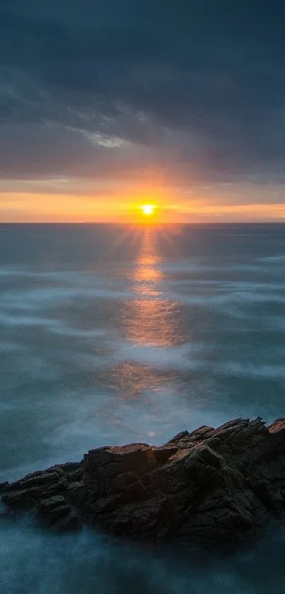 Serene sunset over the ocean with a rocky foreground and vibrant horizon.