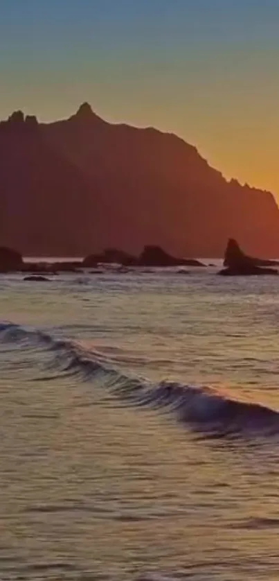 A serene sunset over the ocean with gentle waves and a mountain backdrop.