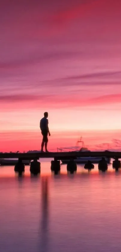 Silhouette on a pier during a pink sunset over calm waters.