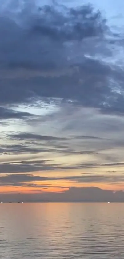 Serene sunset over calm ocean waters with cloudy sky.