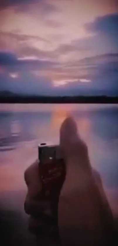 Hand holding lighter against a beautiful sunset over a lake.