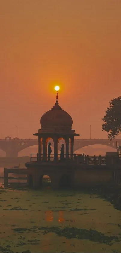 Sunset over river with pavilion silhouette and orange sky.