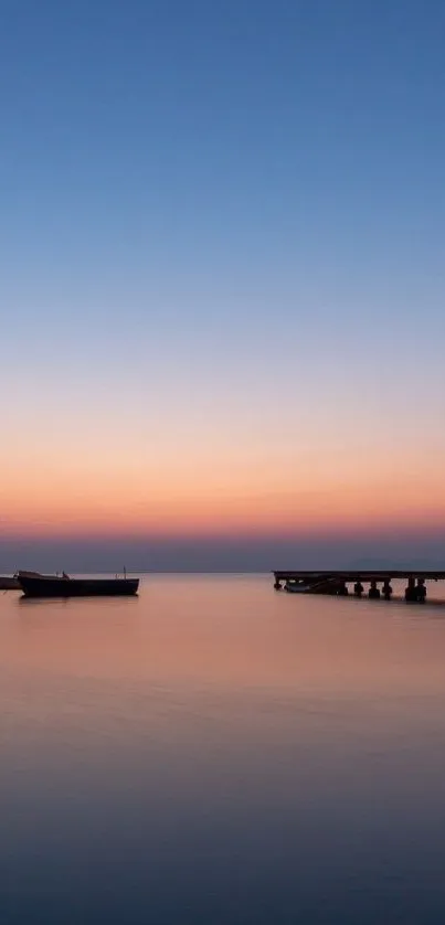 Serene sunset over water with boats and pier silhouetted against colorful sky.