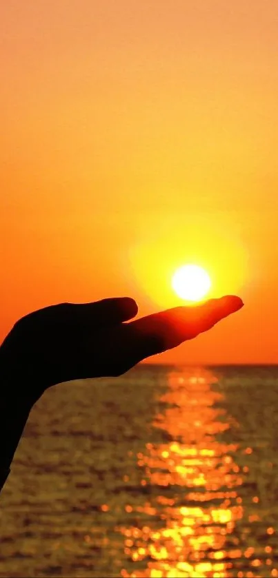 A stunning sunset held in a silhouetted hand over the ocean waves.