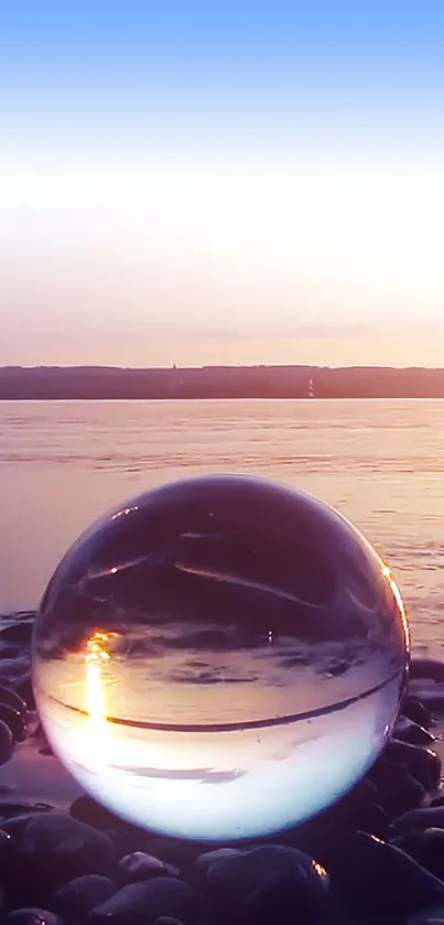 Glass sphere on pebbles reflecting a serene sunset over the ocean.