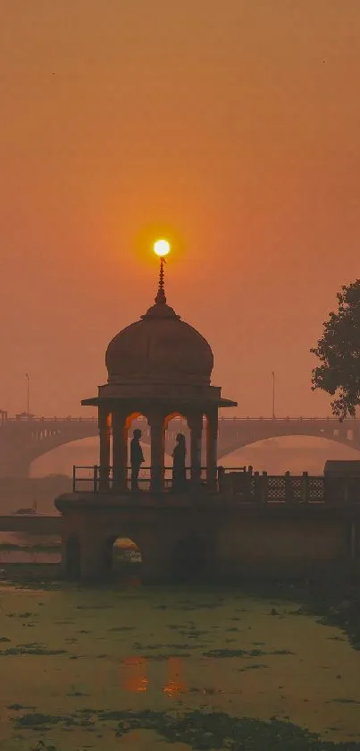 Serene sunset at riverside with gazebo silhouette.